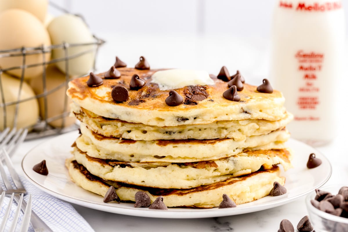 Stack of 5 chocolate chip pancakes on a white plate topped with melted butter.