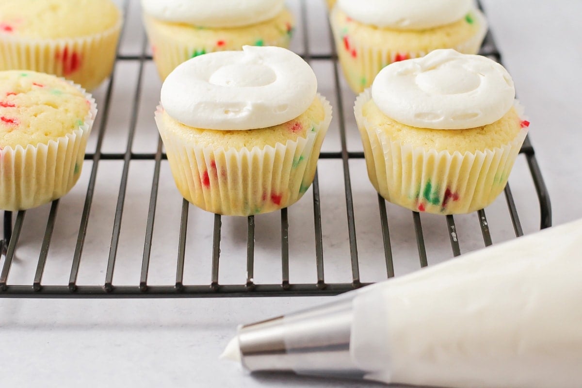 Piping frosting onto cooled cupcakes.