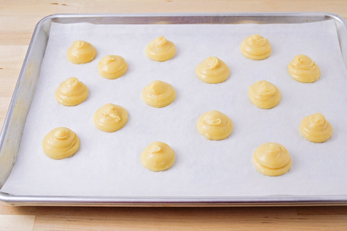 Better than the bakery's, this homemade cream puff recipe proves just how simple and easy it is to create elegant, irresistible pastries! Piped pastry dough on a lined baking sheet.