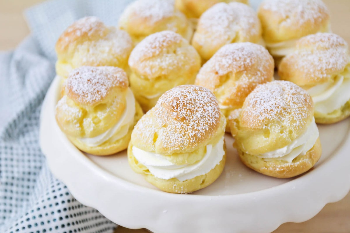 Homemade cream puffs recipe sprinkled with powdered sugar on cake stand.