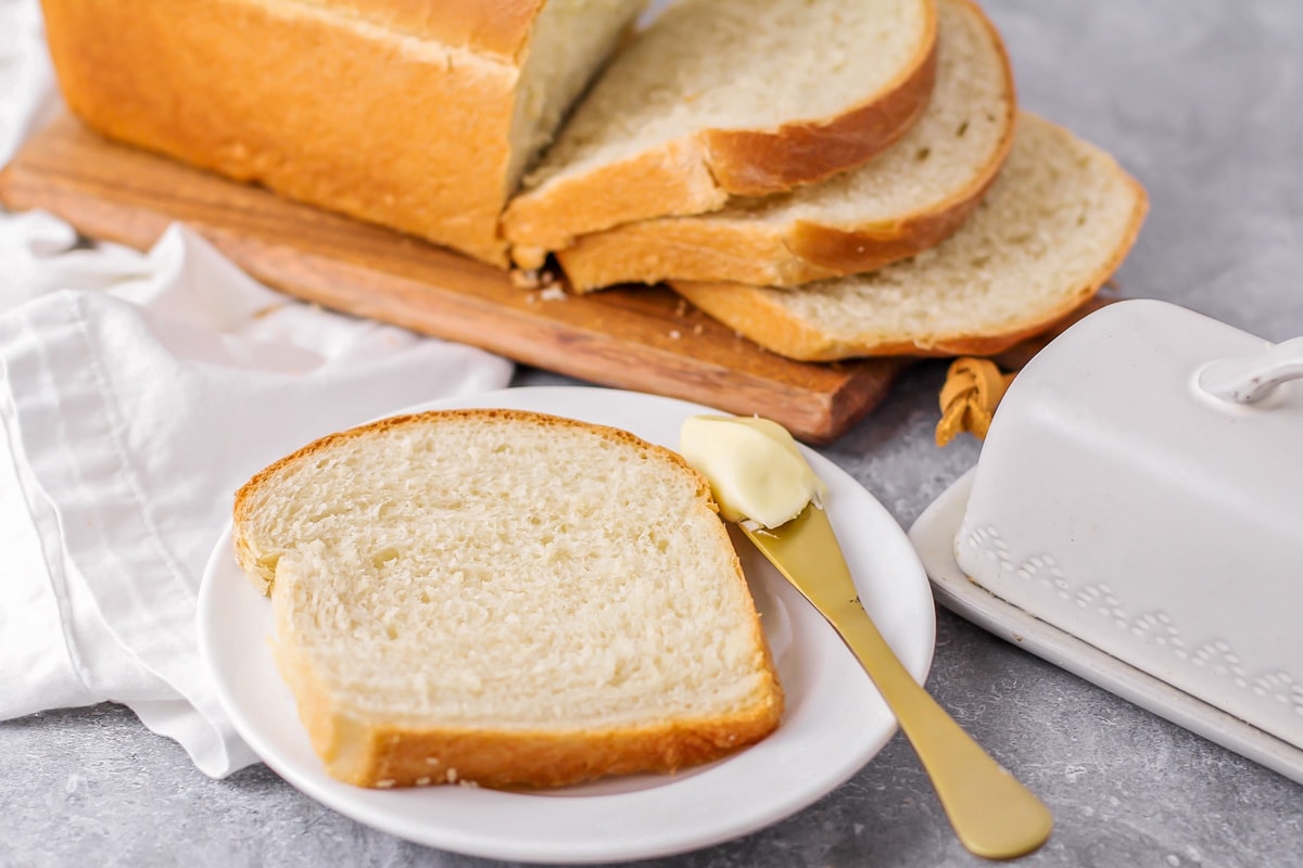 Baked and sliced white bread recipe served on a white plate with butter.
