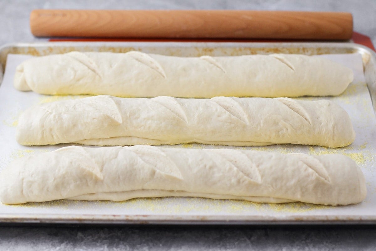 Three loaves of french bread recipe rolled and ready for baking on a sheet pan.
