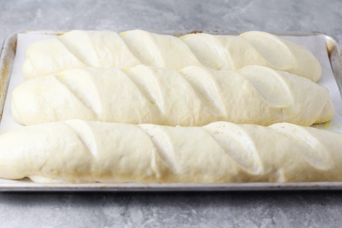 Three loaves of bread ready for baking on a sheet pan.