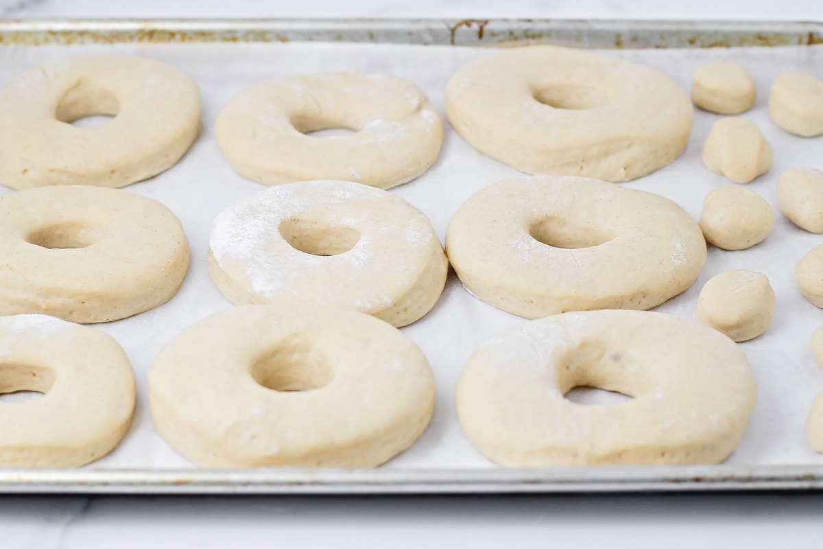Homemade donuts risen on parchment paper lined baking sheet.