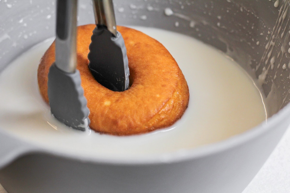 Freshly fried homemade donuts dipping in glaze.