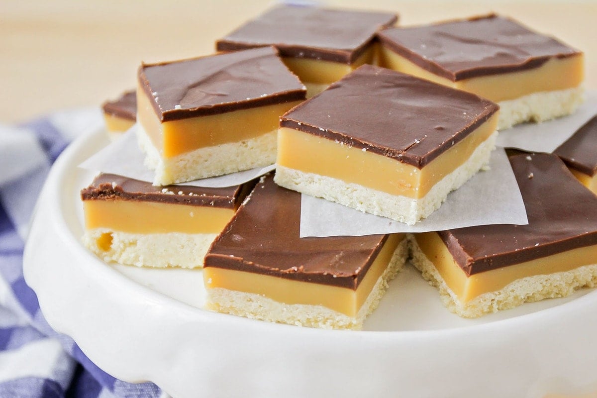 Cookie bar recipes - square cut millionaire bars piled on a white cake stand.