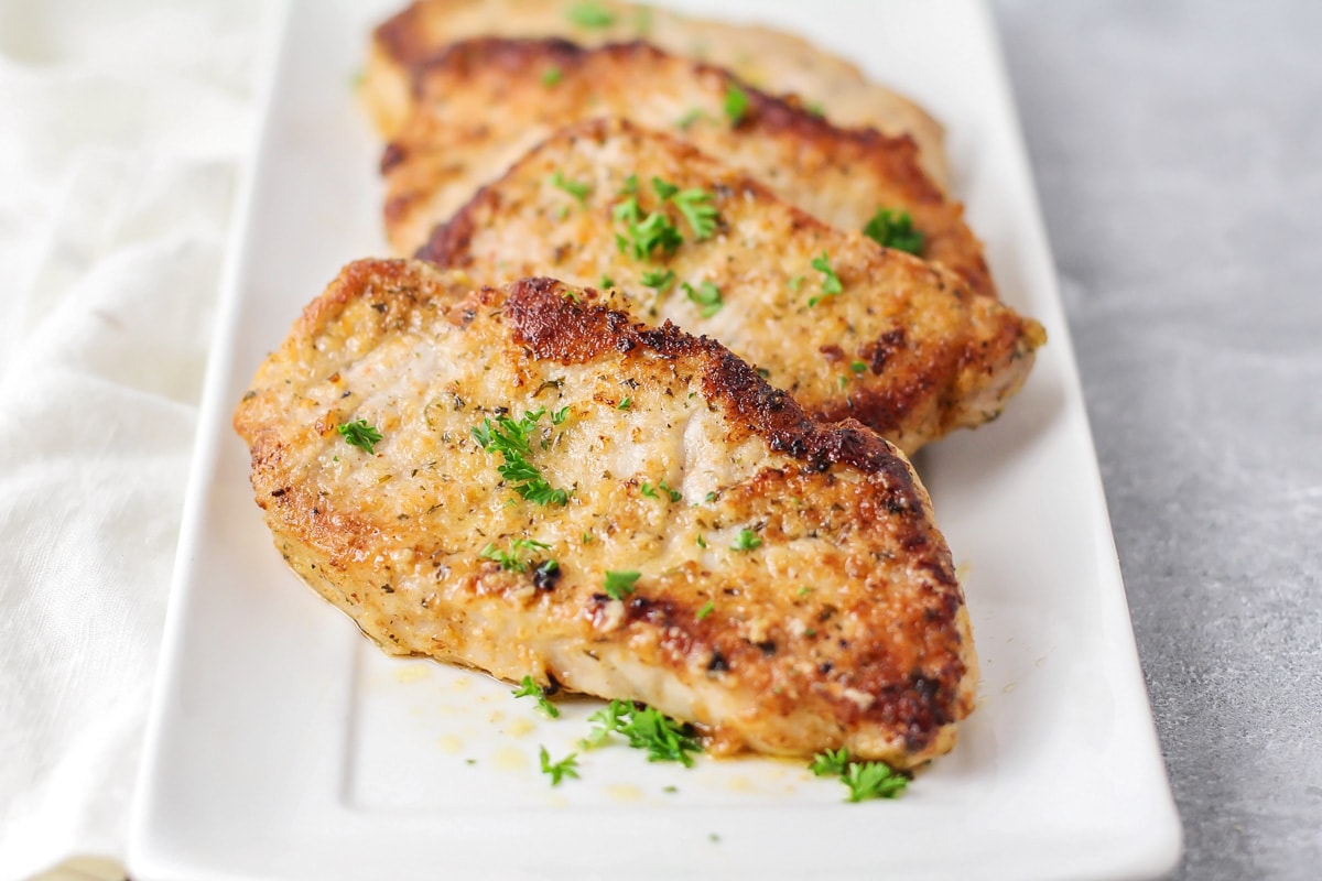 4 pork chops topped with fresh herbs on a white plate.