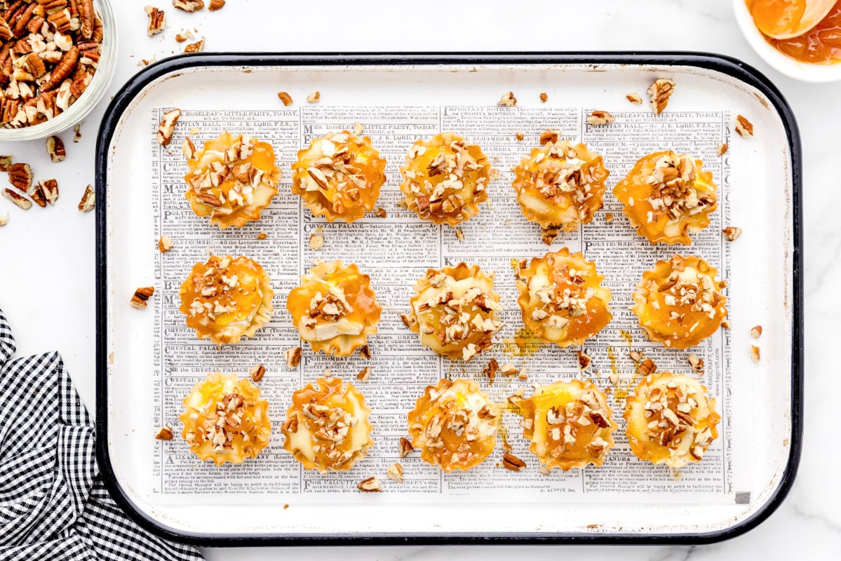 Nuts sprinkled on a pan of freshy assembled brie phyllo tarts.