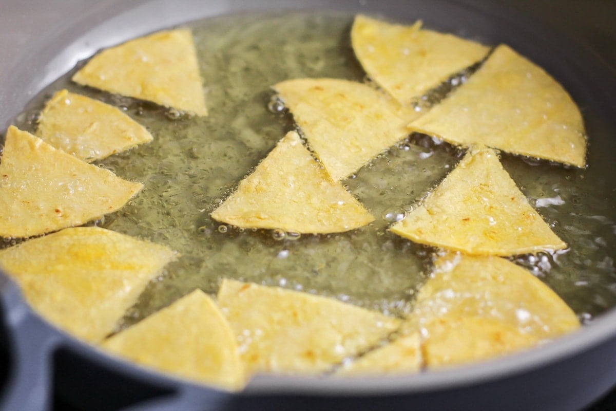 Corn tortilla pieces being fried in oil for homemade tortilla chips.