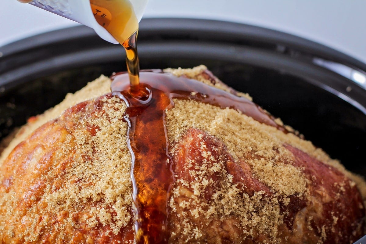 Pouring brown sugar pineapple glaze over crockpot brown sugar ham.