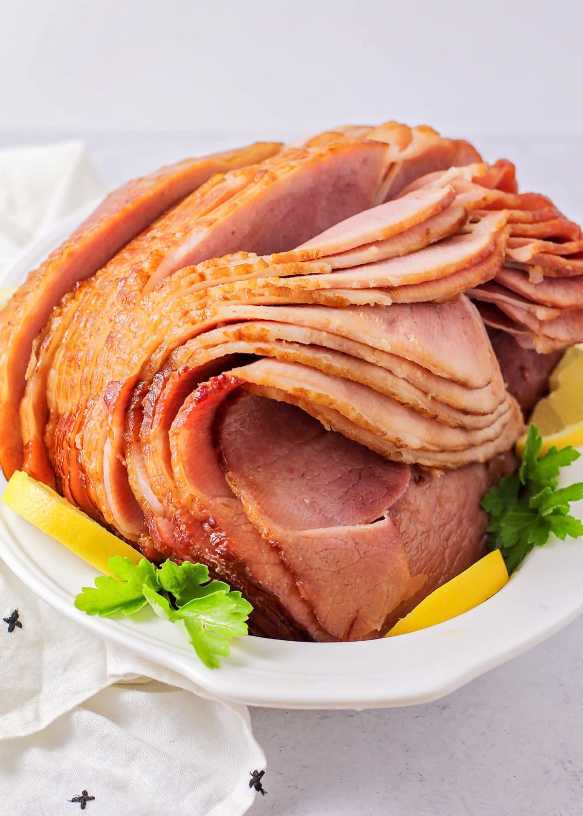 Crockpot ham served with fresh herbs and lemon slices.