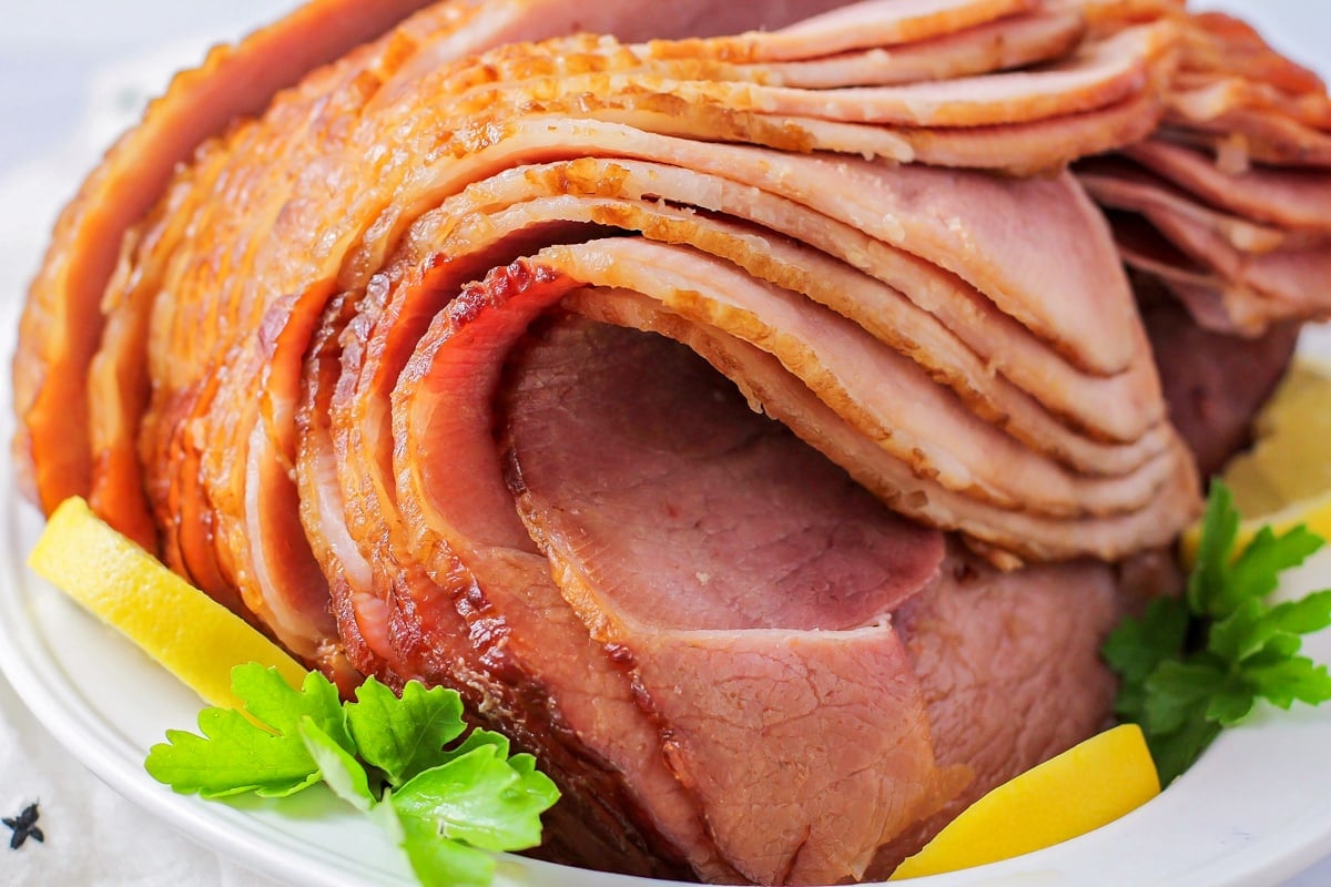 Crockpot brown sugar ham sliced and served with fresh herbs and lemon slices.