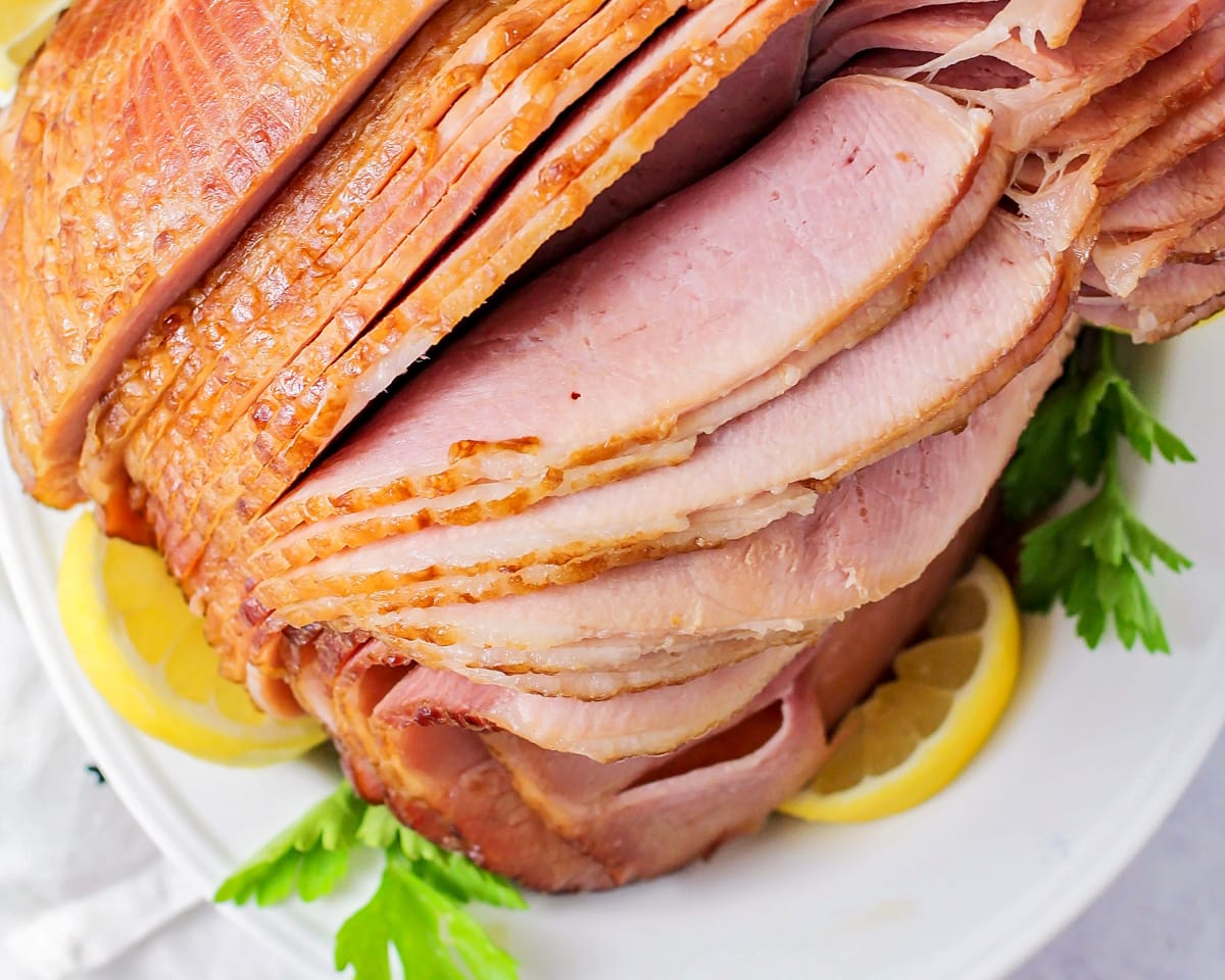 Sliced crockpot brown sugar ham served with fresh herbs and lemon slices.