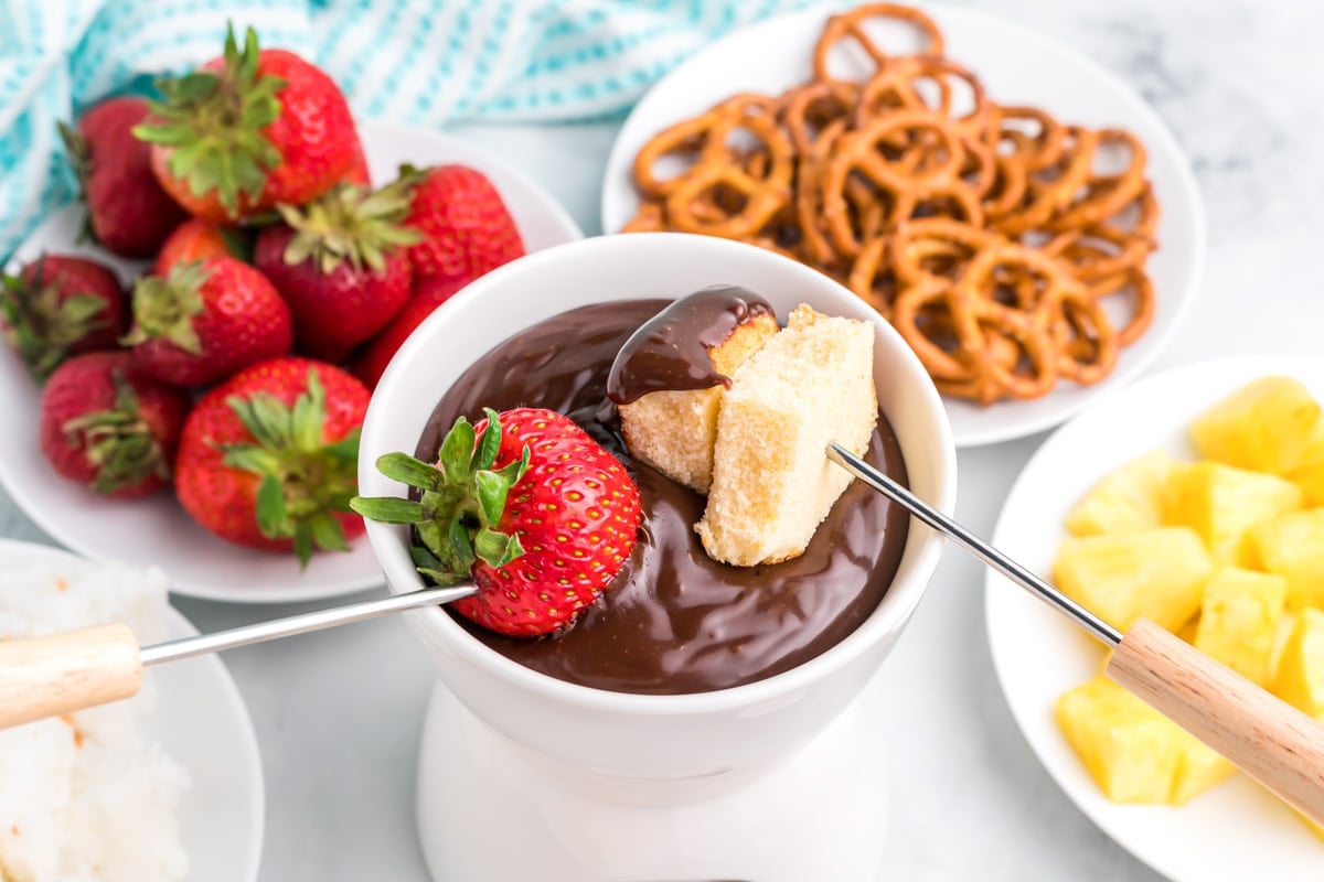 Valentine's Day Desserts - chocolate fondue in a white bowl with a whole strawberry and pound cake on metal skewers being dipped in it. 