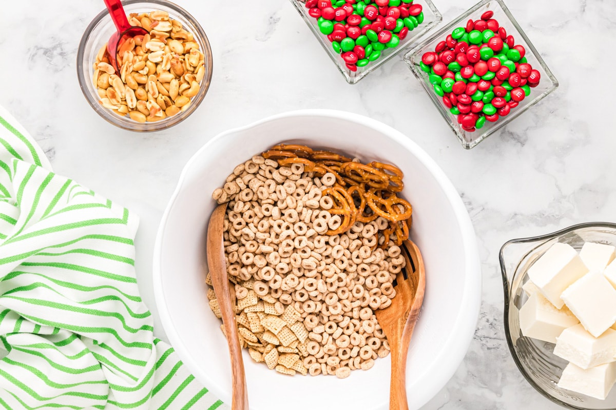 Combining cereal and pretzels for Christmas Chex mix in a white bowl.
