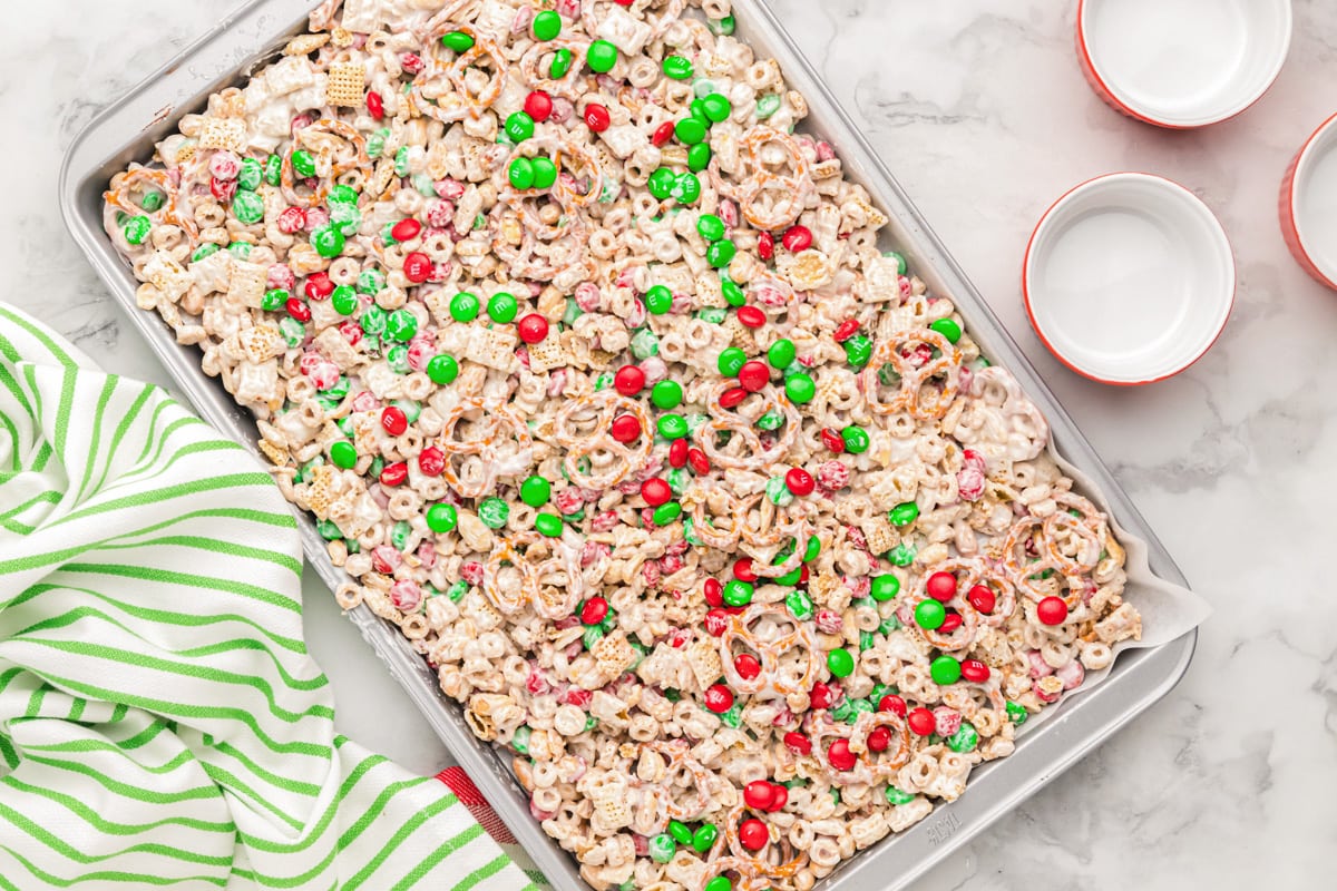 Coated Christmas chex mix spread in a baking sheet to cool.
