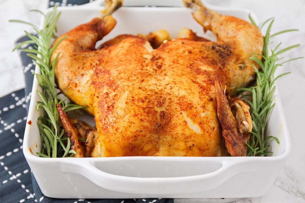 Slow cooker roast chicken on a bed of rosemary in a baking dish.