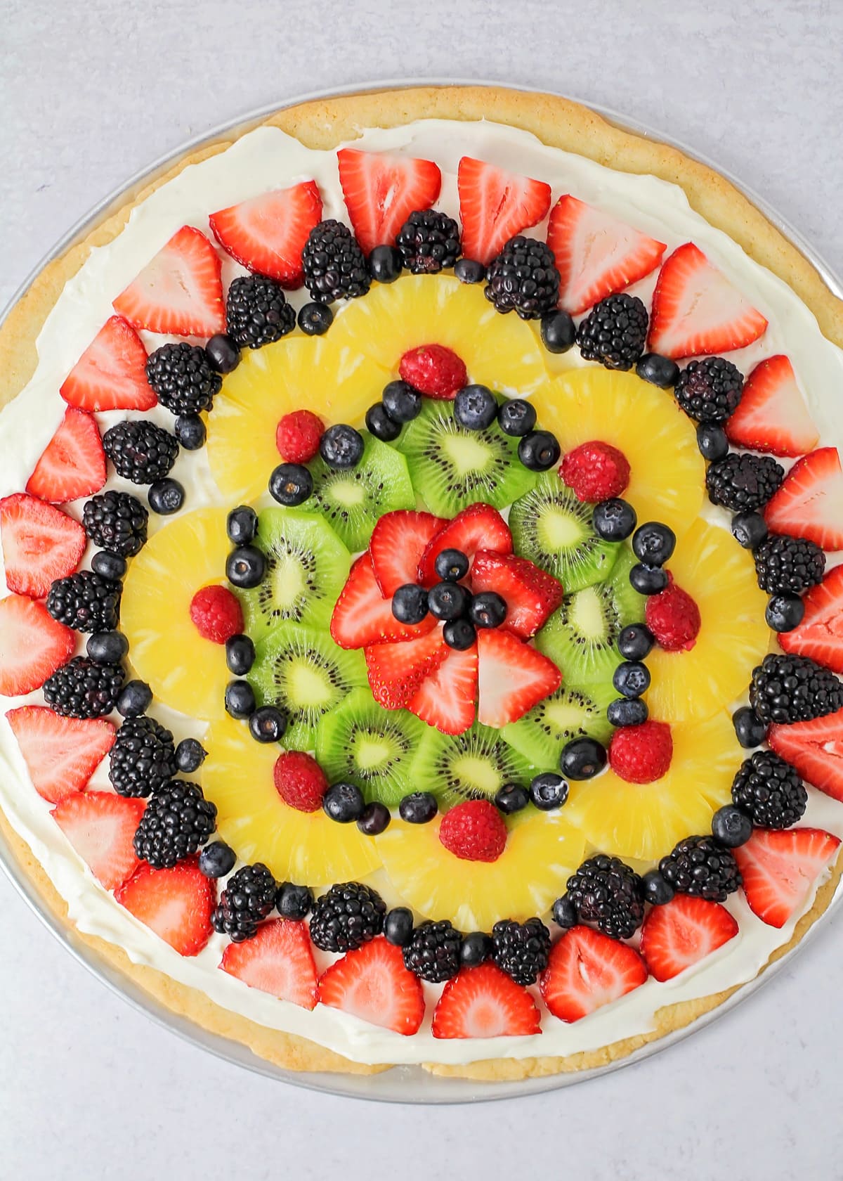 Close up of decorated fruit pizza recipe topped with fruit and berries.