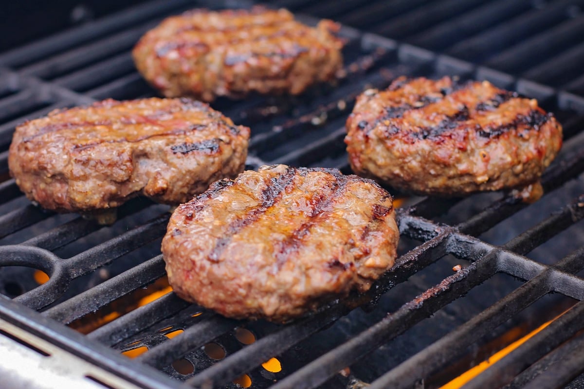 Four hamburger patties cooking on a grill.