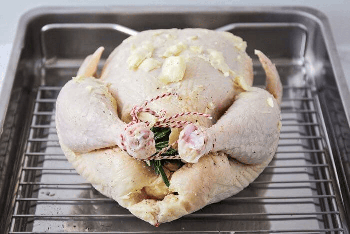 A whole chicken filled with rosemary and topped with butter in a roasting pan.