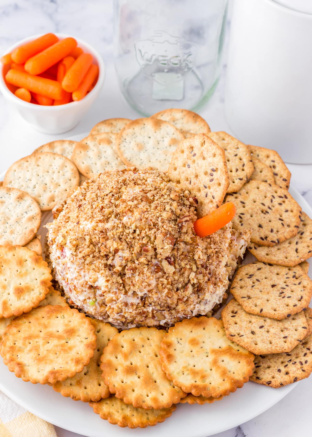 Pineapple cheese ball surrounded by crackers with a carrot stuck in the side.