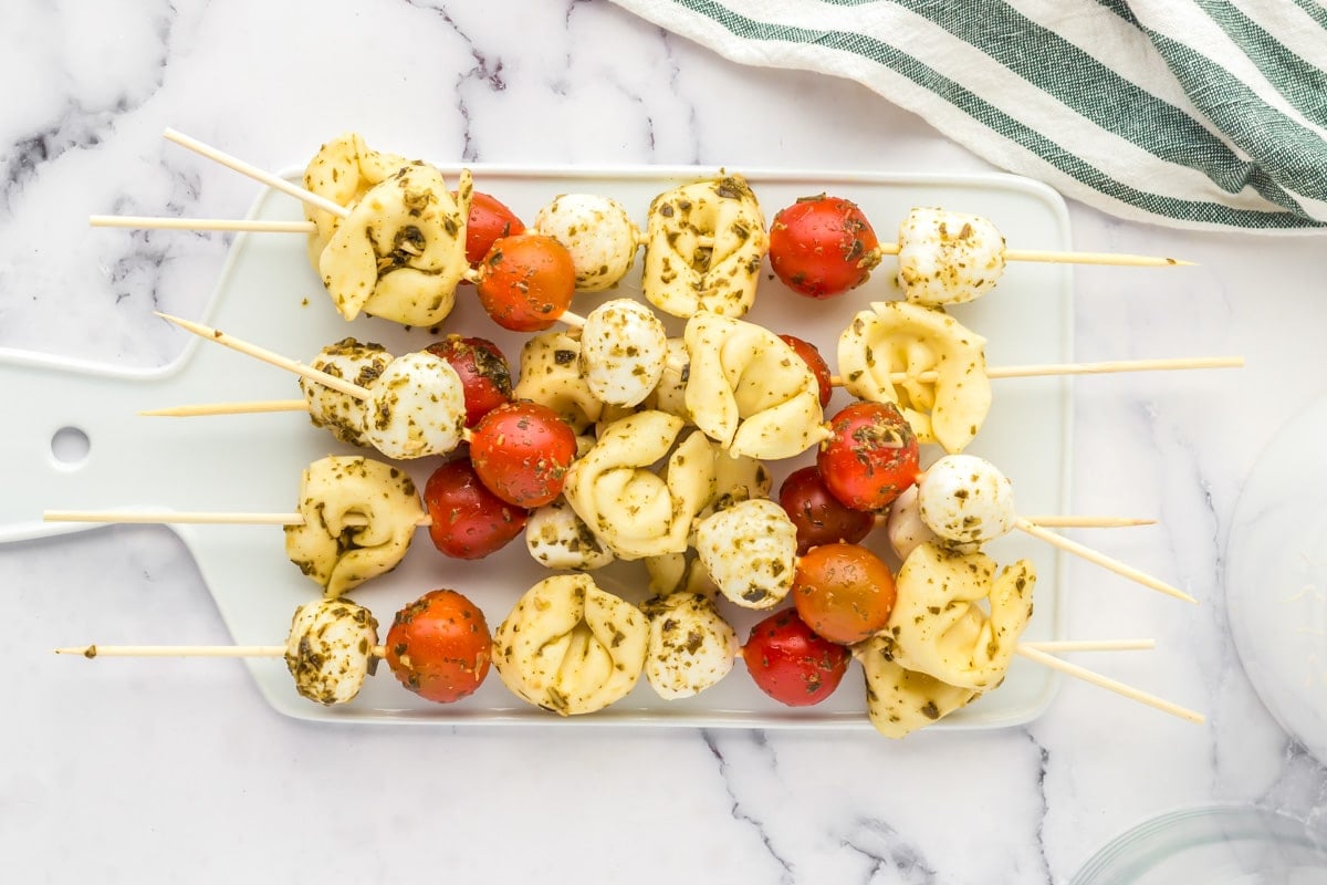 Tortellini skewers piled on a white serving board.