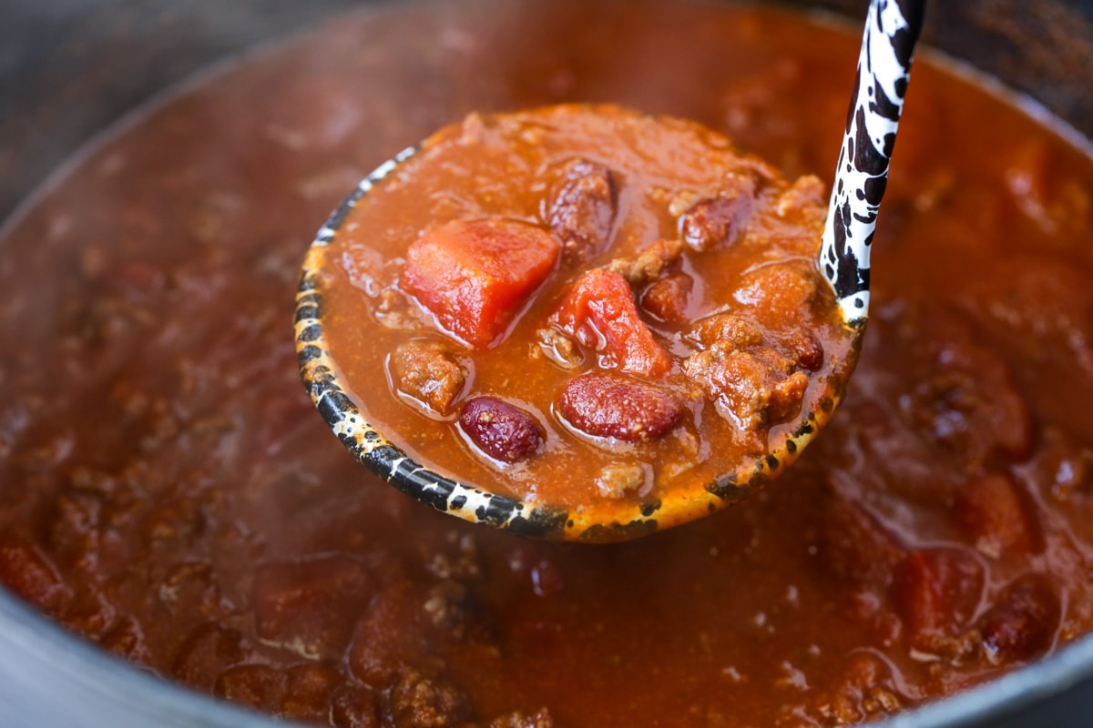 A ladle full of chili over a pot on the stove.