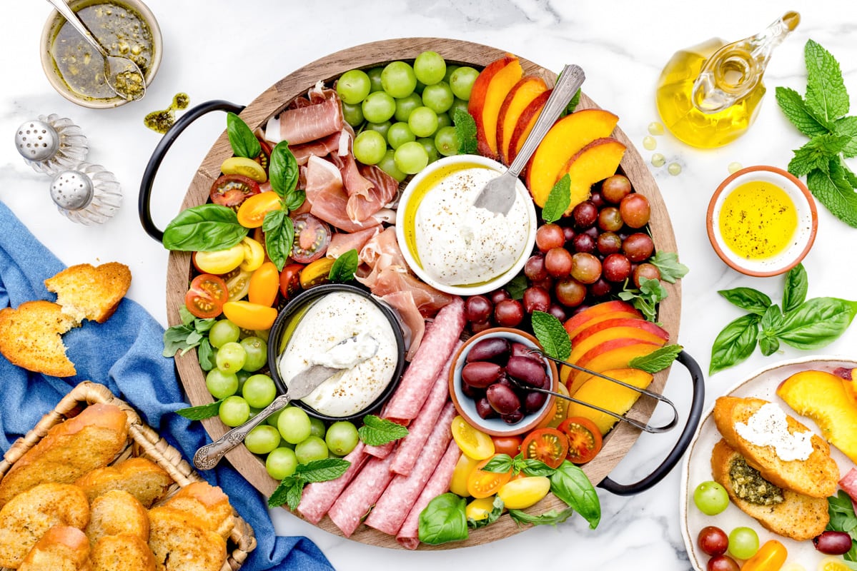 A burrata board spread with many fruits, meats, and veggies.