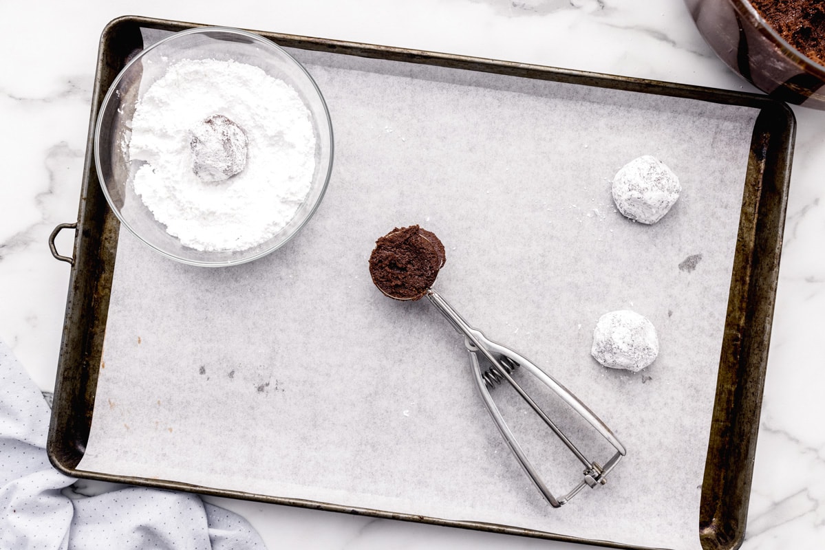 Scooping chocolate crinkle cookies for dipping in powdered sugar.