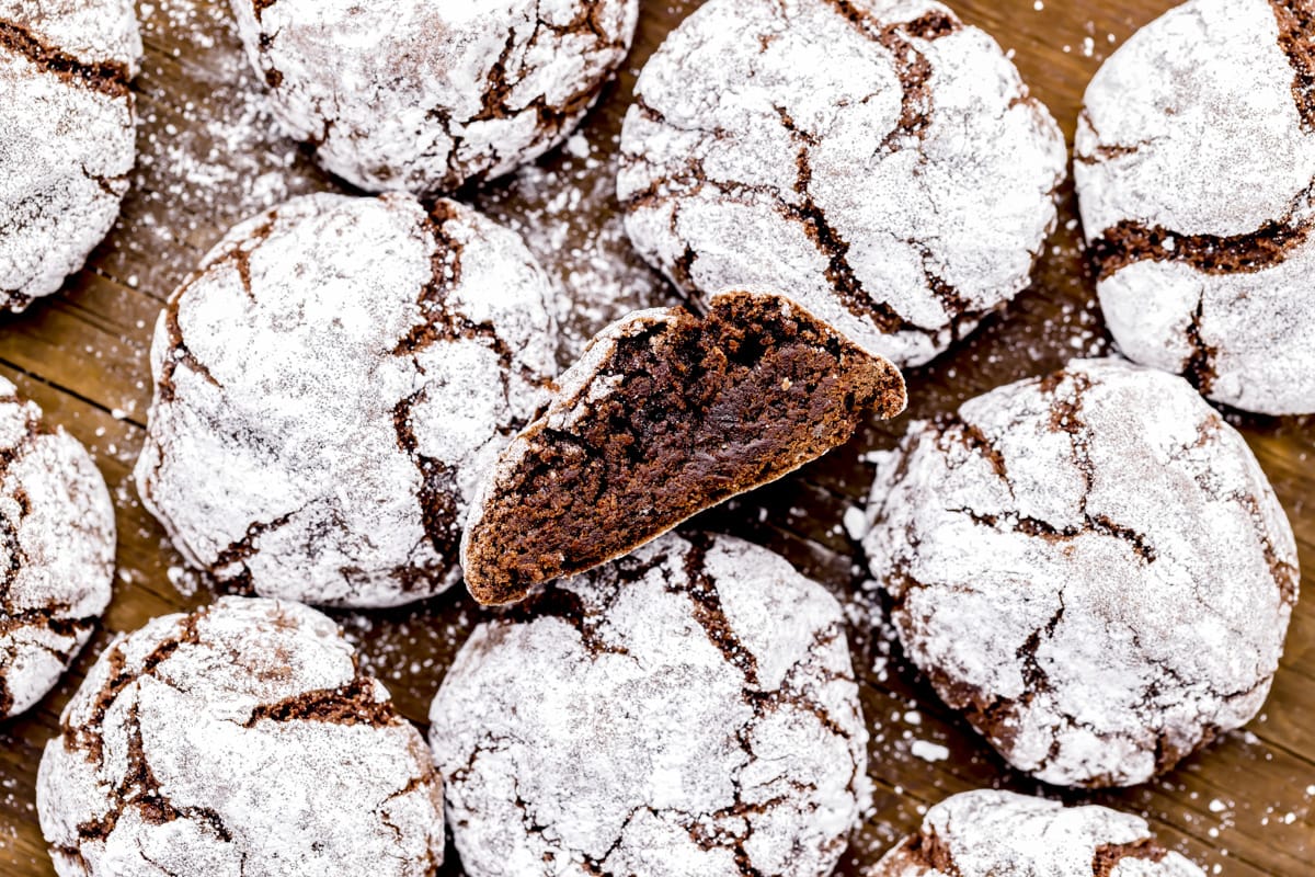 Several chocolate crinkle cookies displayed on a wooden table with one cut in half.