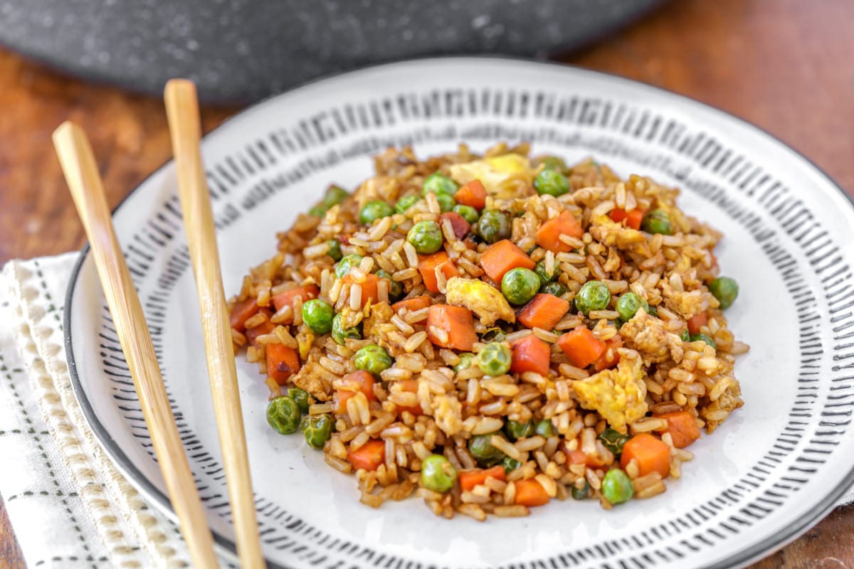 A white plate filled with homemade fried rice with a pair of chopsticks.