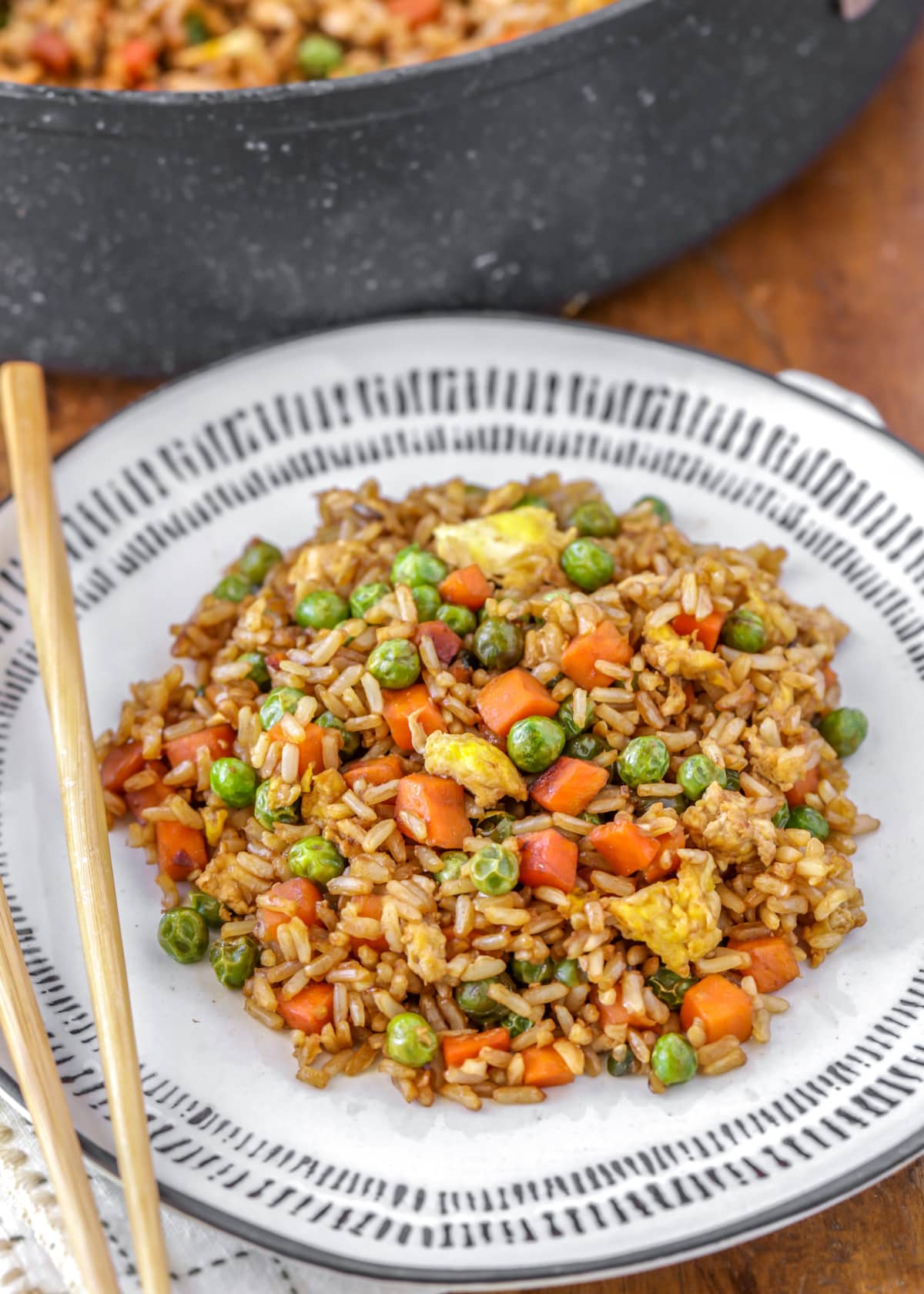 A white plate filled with homemade fried rice and a pair of chopsticks.