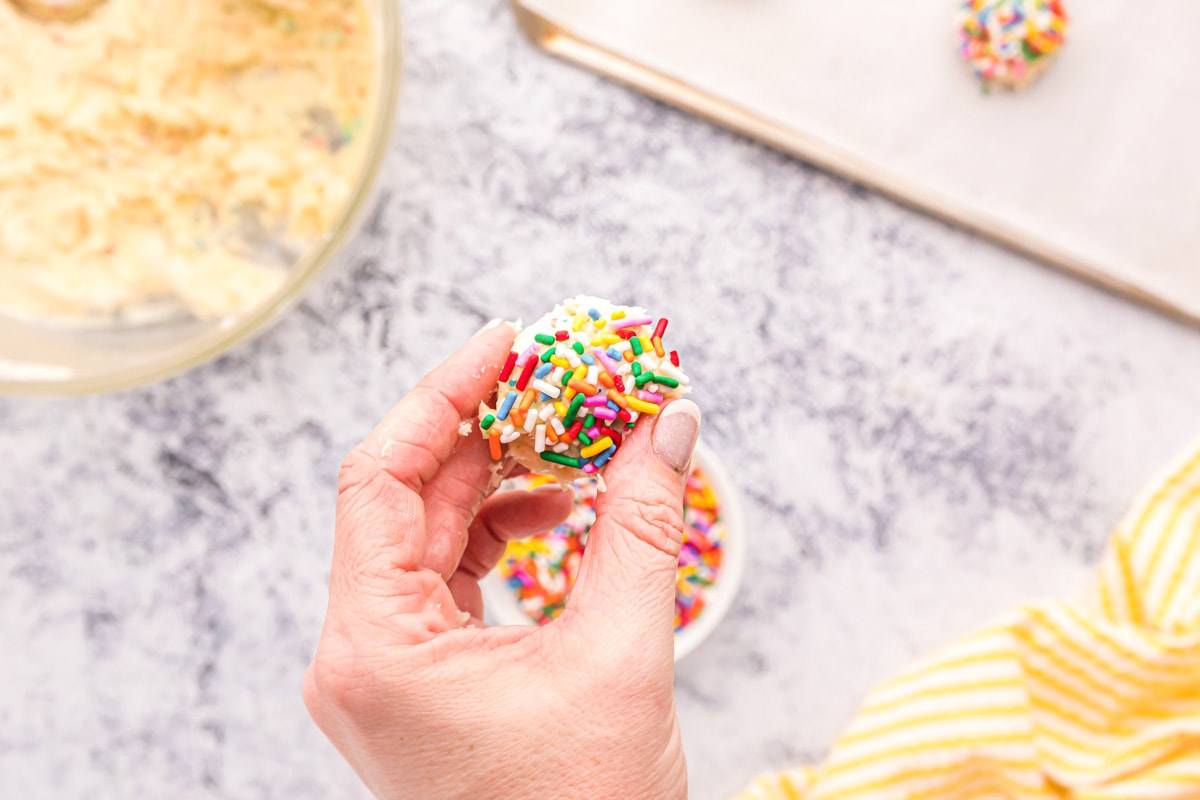 Rolling funfetti cake mix cookies recipe balls in colored sprinkles.