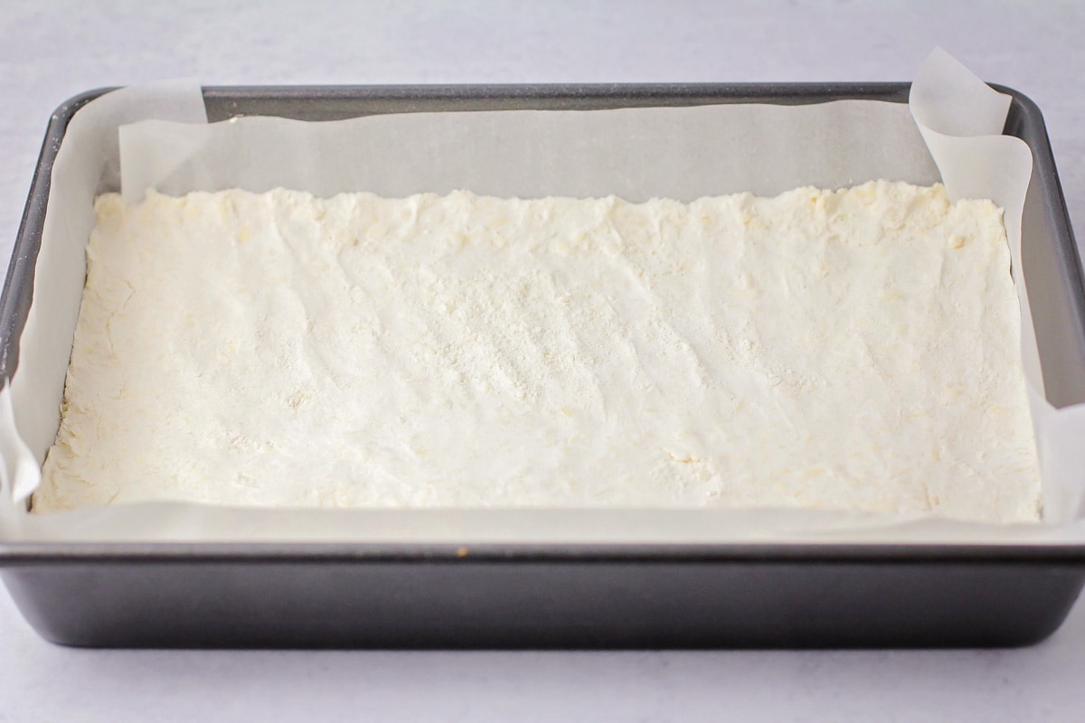Pressing the pecan pie bar crust into a pan.