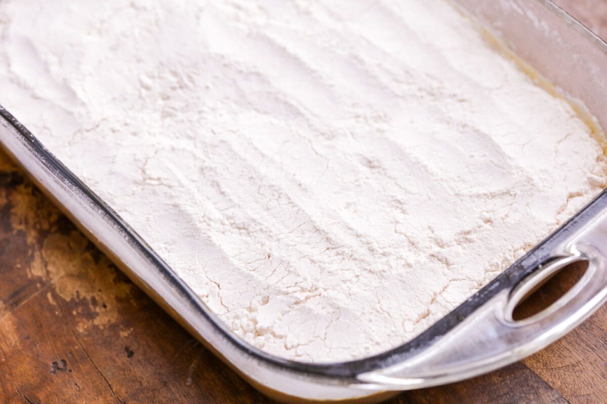 Cake mix poured over pumpkin cake batter in a baking dish.