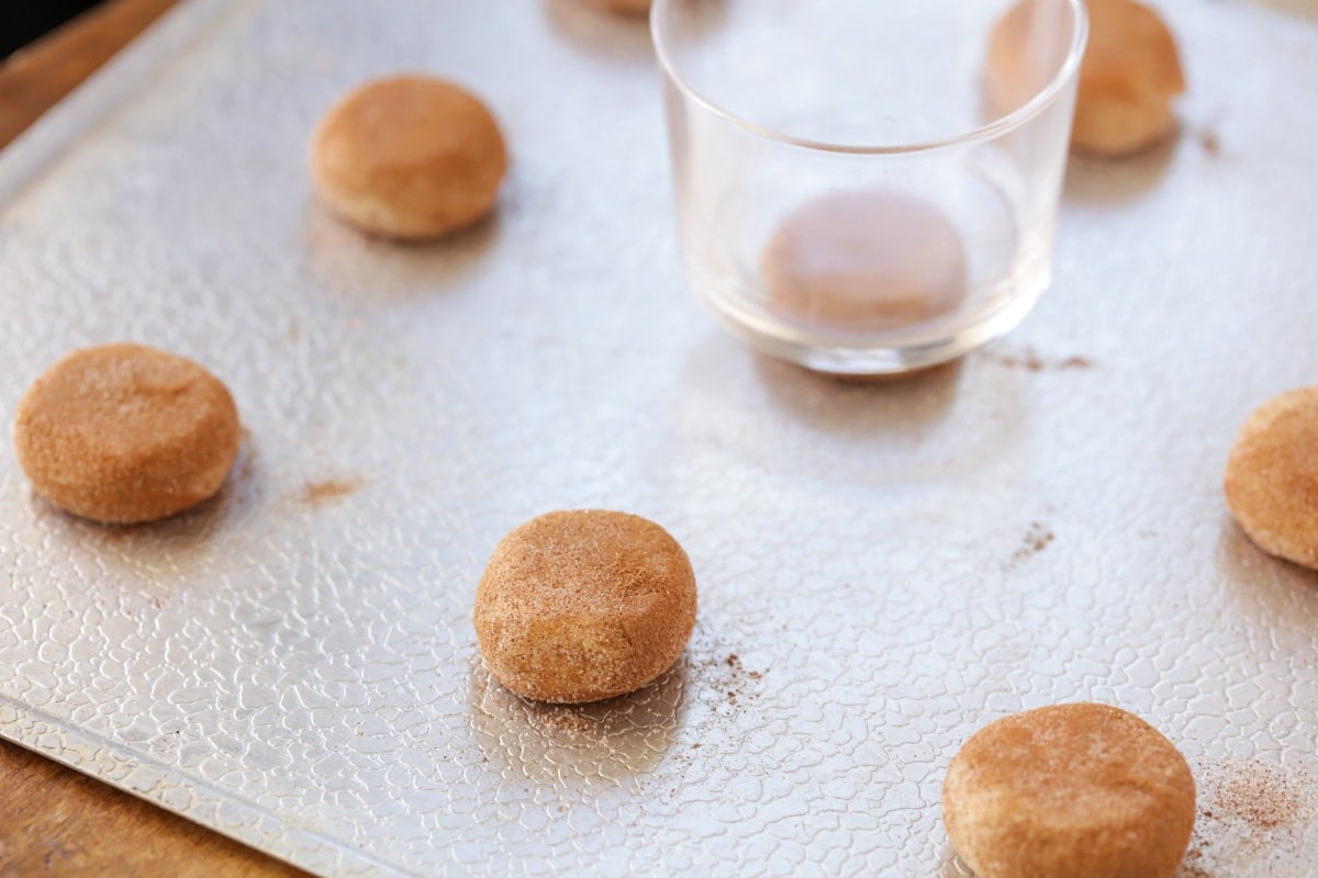 Pressing snickerdoodle cookies dough balls with a glass.
