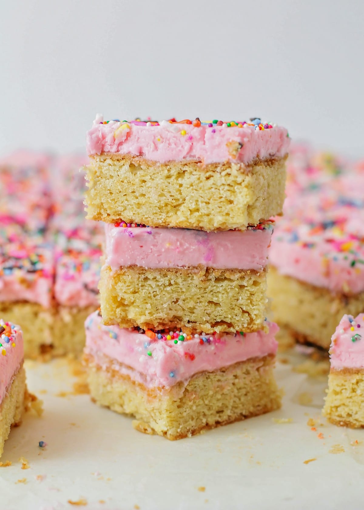 Frosted sugar cookie bars stacked and covered with sprinkles.