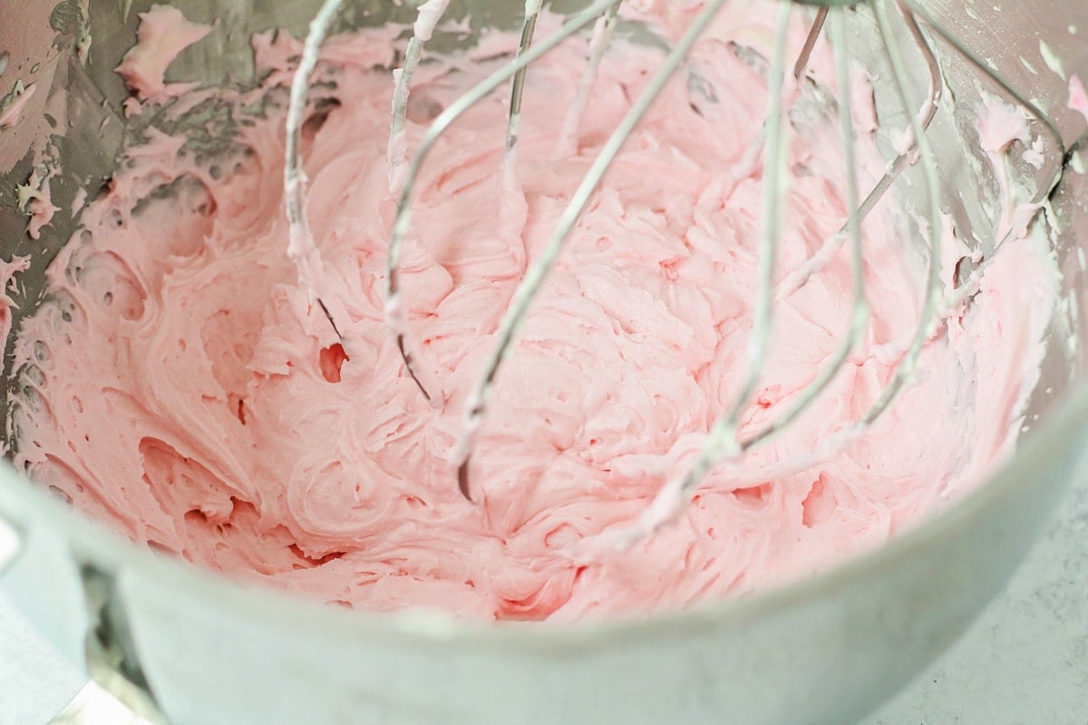 Mixing pink frosting for sugar cookie bars in a metal bowl.