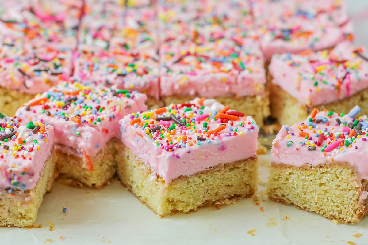 Several sugar cookie bars frosting with pink frosting and colored sprinkles.