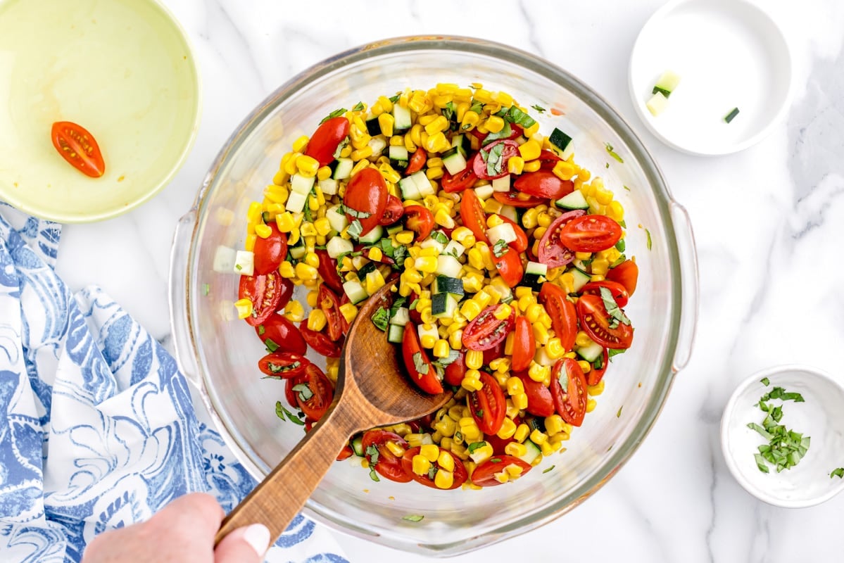 Mixing summer corn salad ingredients in a bowl.