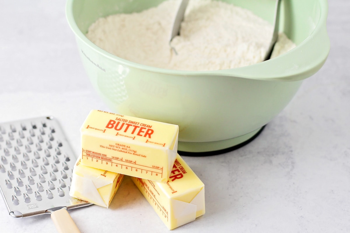 Butter sticks next to a bowl of flour.