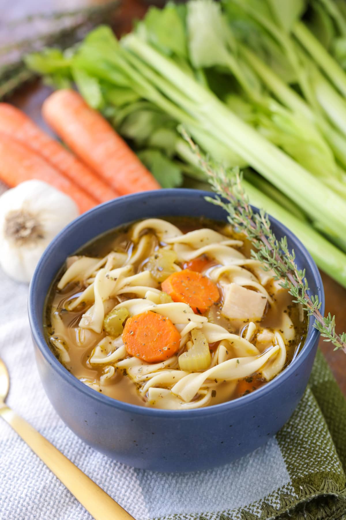 A bowl filled with homemade chicken noodle soup topped with a sprig of rosemary.