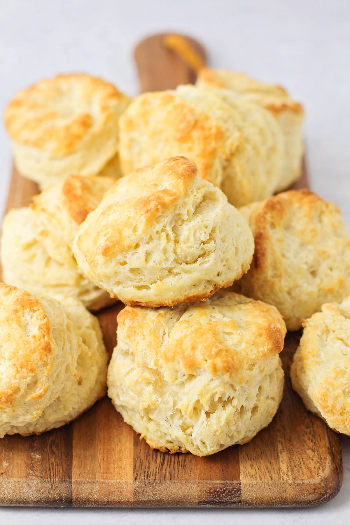 Homemade biscuits piled on a wooden cutting board.