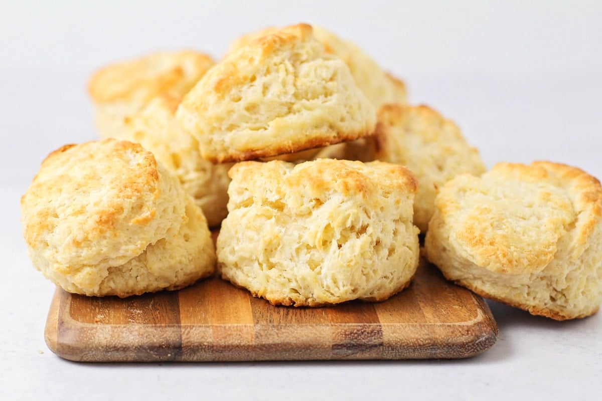 Homemade biscuits stacked on a wooden cutting board.