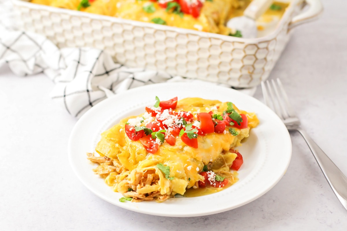 Honey Lime Chicken Enchiladas topped with diced tomatoes, chopped cilantro and crumbled cotija cheese on a white plate. 