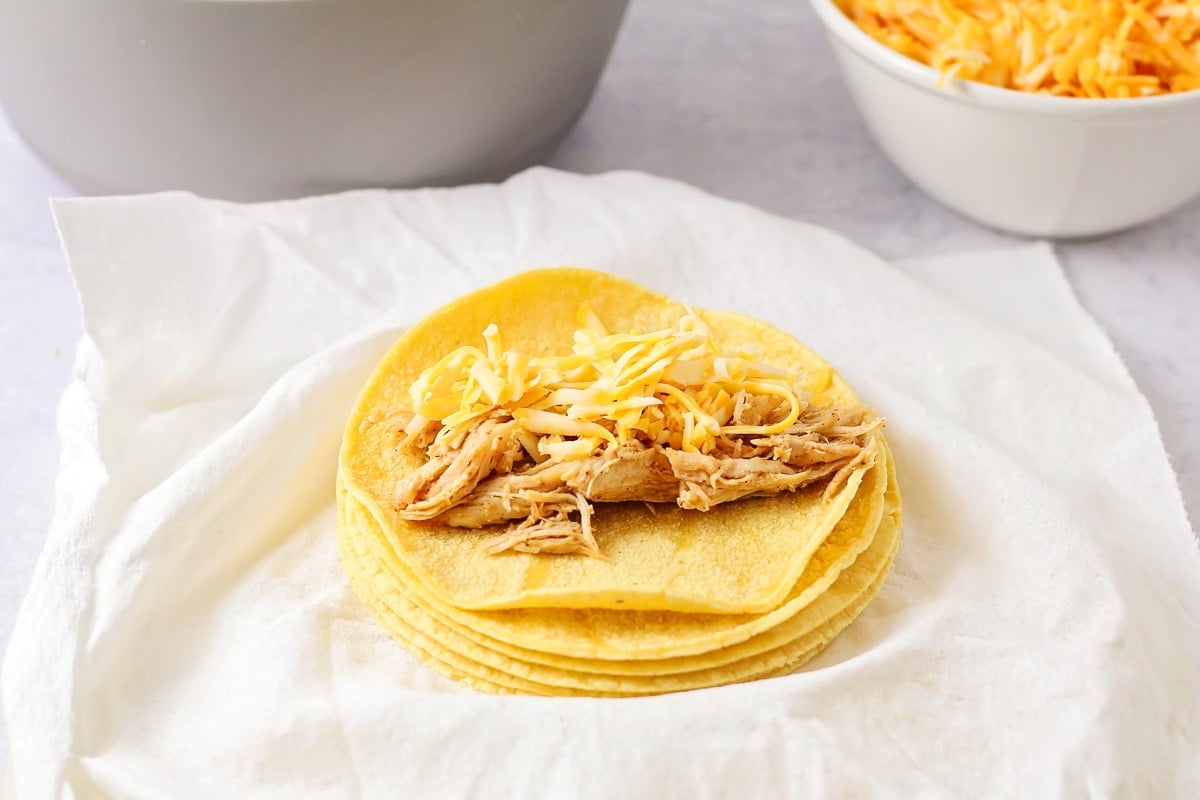Placing chicken on tortillas for honey lime chicken enchiladas.