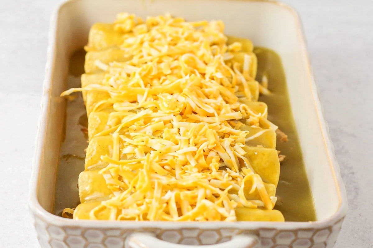 A baking dish of honey lime chicken enchiladas topped with cheese.