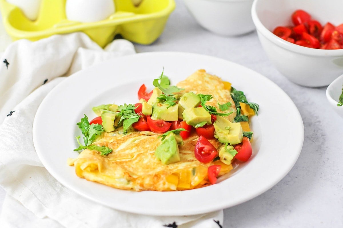 Easy Breakfast Ideas - Omelette topped with diced avocado, diced cherry tomatoes and parsley flakes on a white plate. 