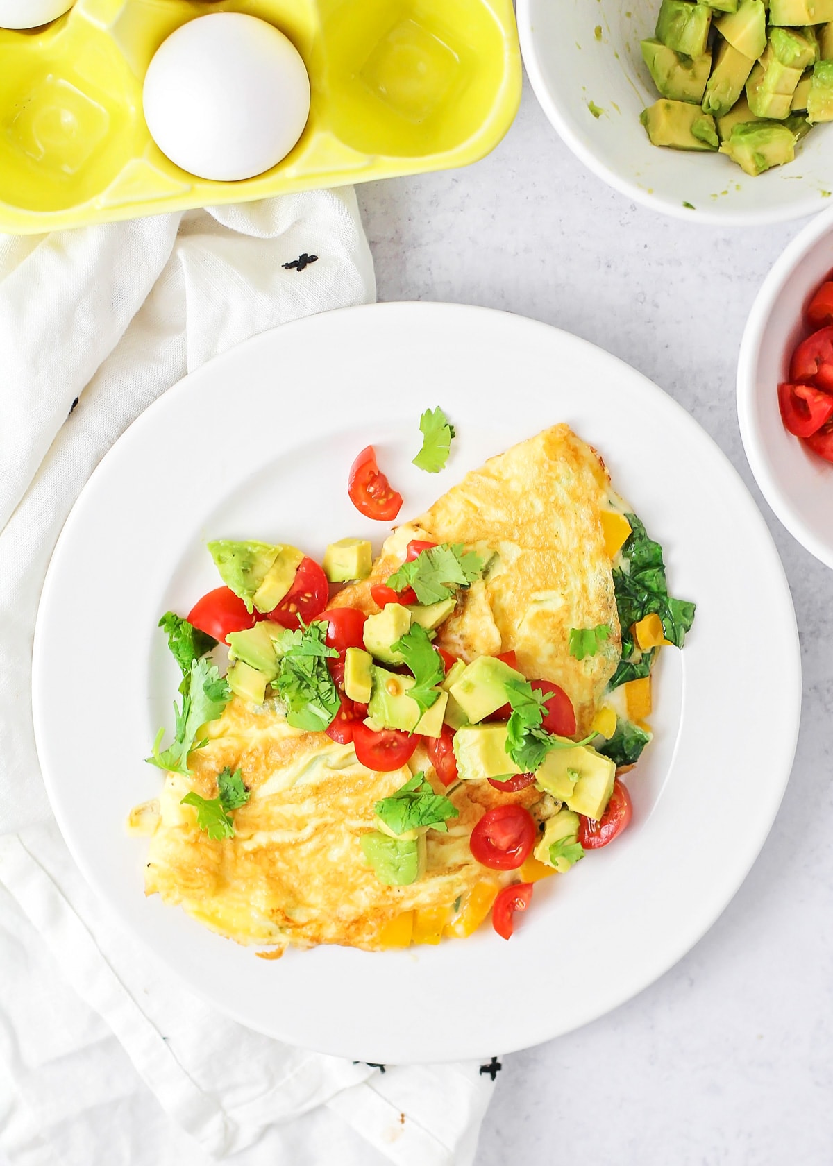 A cooked omelette topped with avocado, tomato, and cilantro.