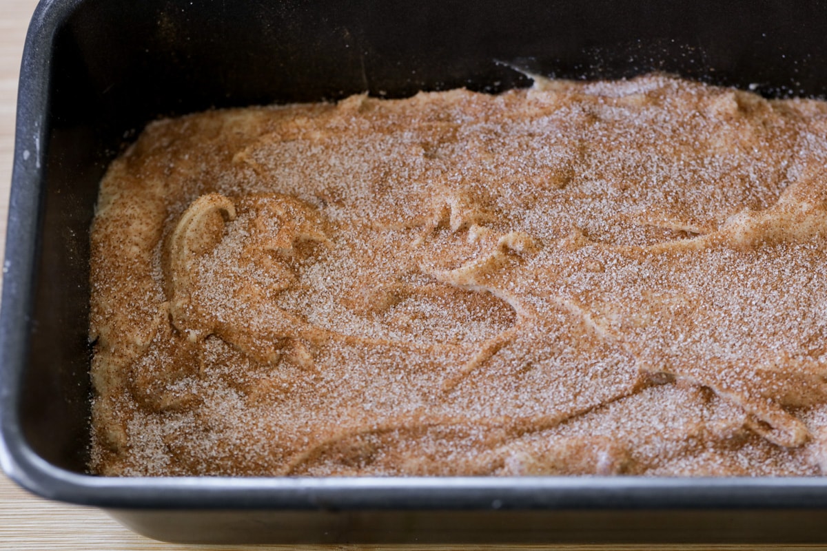 Snickerdoodle bread batter in a pan sprinkled with cinnamon-sugar mixture.